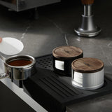 Black and silver filter paper holders on a tamping mat with a portafilter and tamper