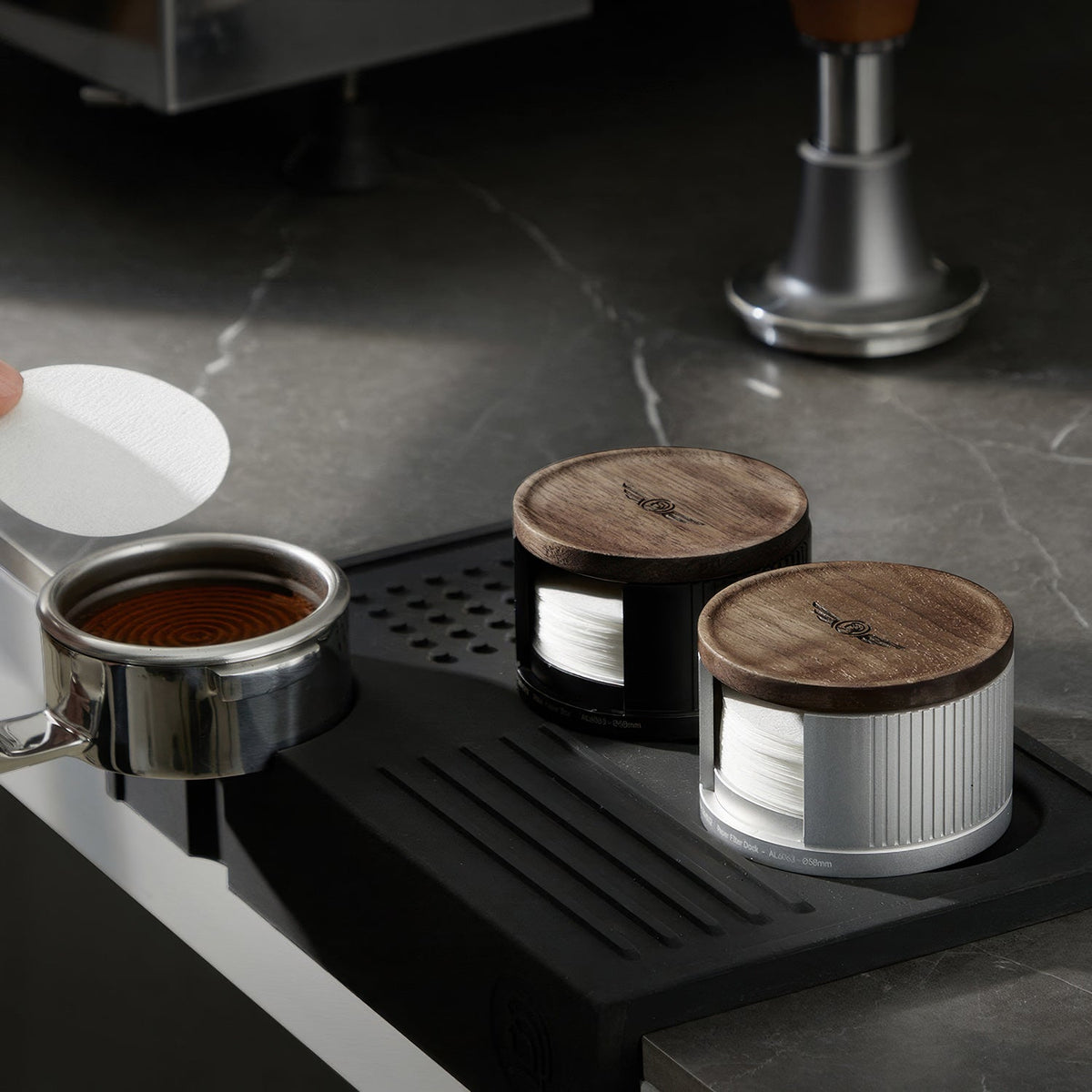 Black and silver filter paper holders on a tamping mat with a portafilter and tamper