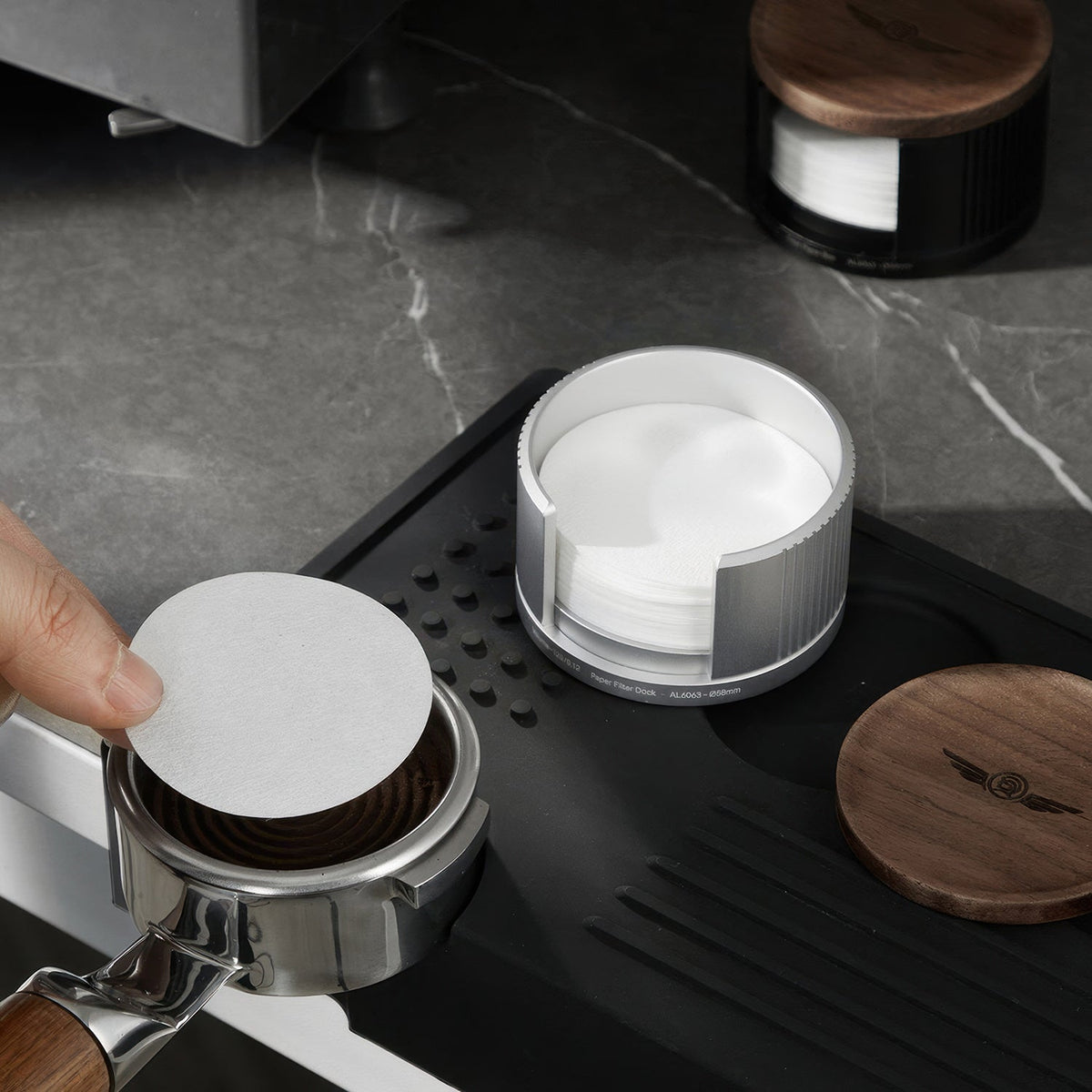 Placing a paper filter on a tamped espresso puck, holder and walnut lid alongside